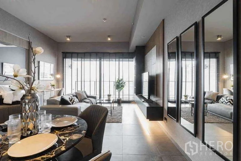 Condominium for rent in Watthana, Bangkok - Bright living room with large glazing, wall-mounted TV, mirrored feature wall and balcony access.