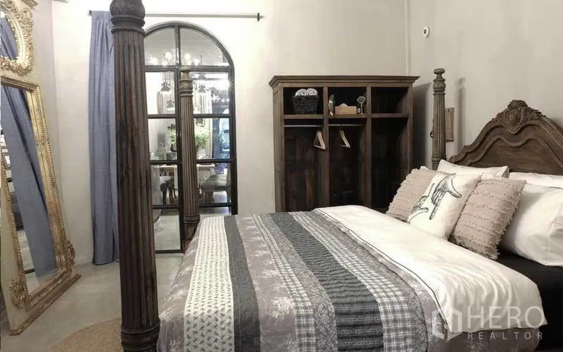 Townhouse for rent in Watthana, Bangkok - Bedroom with carved wooden bed, arched glass door and tall ornate mirror.