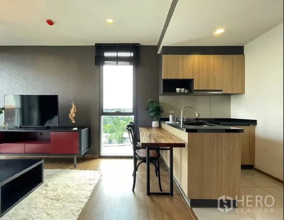 Condominium for rent in Watthana, Bangkok - Open-plan living area with TV unit, rug, and wood kitchen with a breakfast bar.