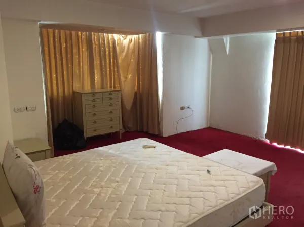 Condominium for rent in Khlong Toei, Bangkok - Second bedroom with red carpet, cream curtains and a dresser by a bay-style window.