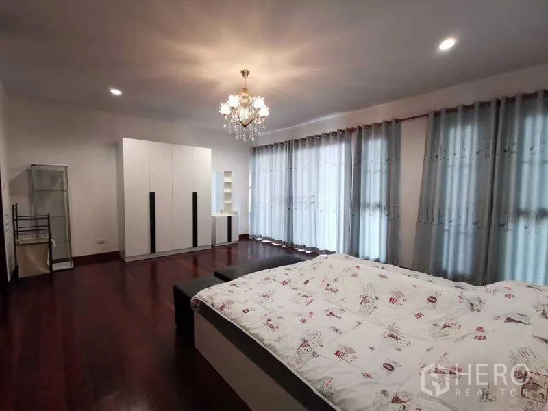 บ้าน ให้เช่าในPrawet, Bangkok - ห้องนอนกว้าง โคมไฟระย้า ผนังกระจกยาว ผ้าม่านสีเทา และตู้เสื้อผ้าสีขาวบนพื้นไม้