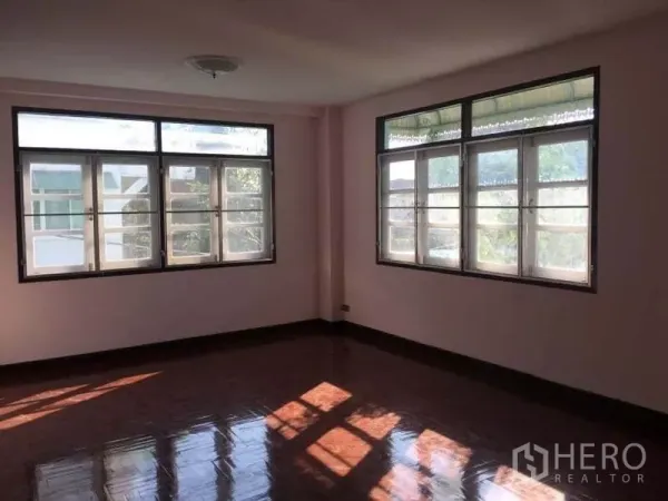Detached House for rent in Chatuchak, Bangkok - Corner bedroom with two walls of windows and dark wood floors.