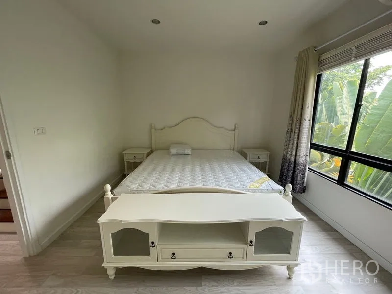 Townhouse for rent in Bang Kapi, Bangkok - Master bedroom with white furniture, bed and large window facing tropical greenery.