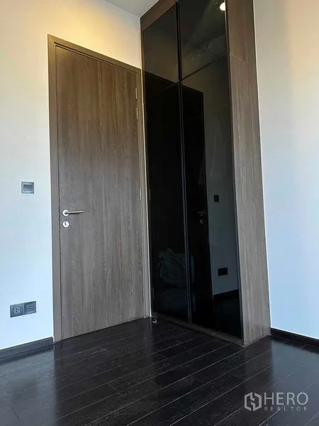 Condominium for rent in Khlong Toei, Bangkok - Entry corner with wooden door and sleek black built-in wardrobe in condominium.