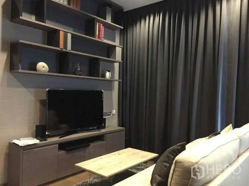 Condominium for rent in Bang Rak, Bangkok - Modern living room in Bang Rak condo with TV console and open shelves beside floor-to-ceiling blackout curtains.