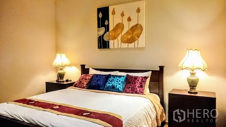 Condominium for rent in Khlong Toei, Bangkok - Cozy bedroom with king bed, bedside lamps and framed artwork above the headboard.