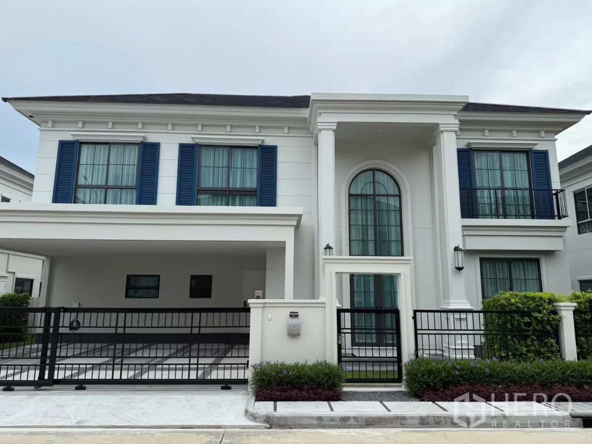บ้าน ให้เช่าหรือขายในBang Phli, Samut Prakan - ด้านหน้าบ้านเดี่ยวสองชั้นสไตล์โมเดิร์นคลาสสิก มีบานเกล็ดสีน้ำเงิน ซุ้มประตูโค้ง และโรงจอดรถมีรั้ว
