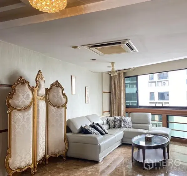 公寓 出租在Khlong Toei, Bangkok - 会客角落，转角沙发、金色装饰屏风与宽大窗户。