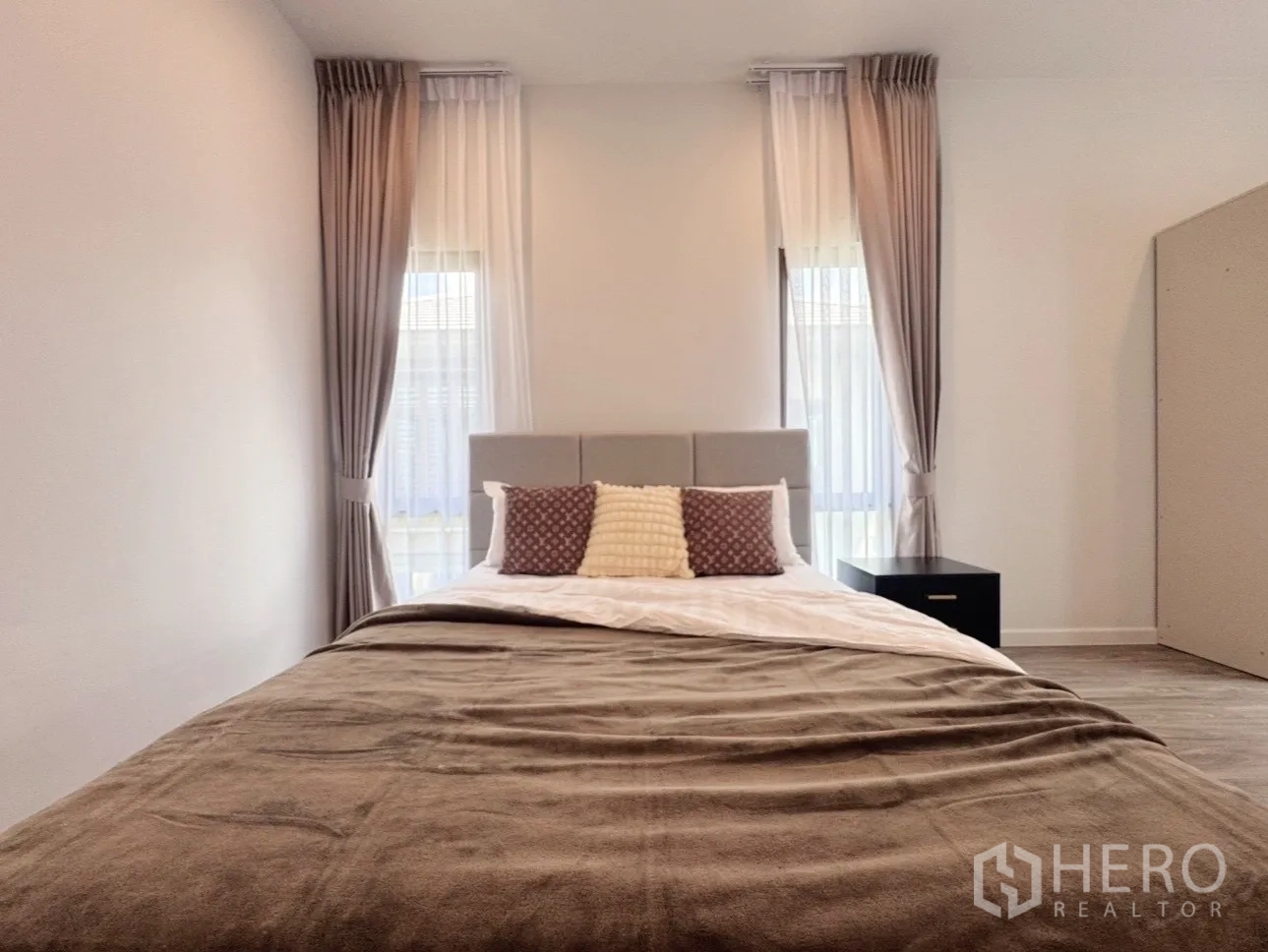 Detached House for rent or sale in Bang Kapi, Bangkok - Guest bedroom front view with bed centered between two tall windows.