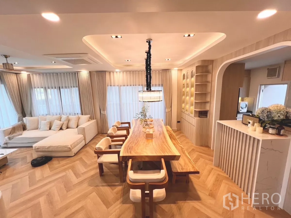 独立式住宅 出租在Bang Phli, Samut Prakan - 宽敞客厅与长餐桌，通高窗帘与内置展示柜