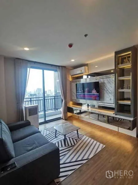 คอนโด ขายในHuai Khwang, Bangkok - ห้องนั่งเล่นสว่าง โซฟา ผนังทีวีบิลต์อิน พื้นไม้ และประตูกระจกบานเลื่อนออกไประเบียงวิวเมือง