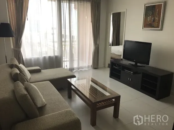คอนโด ให้เช่าในRatchathewi, Bangkok - ห้องนั่งเล่นโปร่ง โล่งด้วยโซฟาเข้ามุม ตู้ทีวี โต๊ะกลางกระจก และประตูบานเลื่อนเปิดสู่ระเบียง