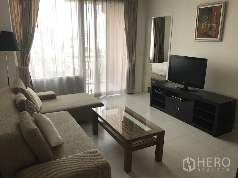 คอนโด ให้เช่าในRatchathewi, Bangkok - ห้องนั่งเล่นโปร่ง โล่งด้วยโซฟาเข้ามุม ตู้ทีวี โต๊ะกลางกระจก และประตูบานเลื่อนเปิดสู่ระเบียง