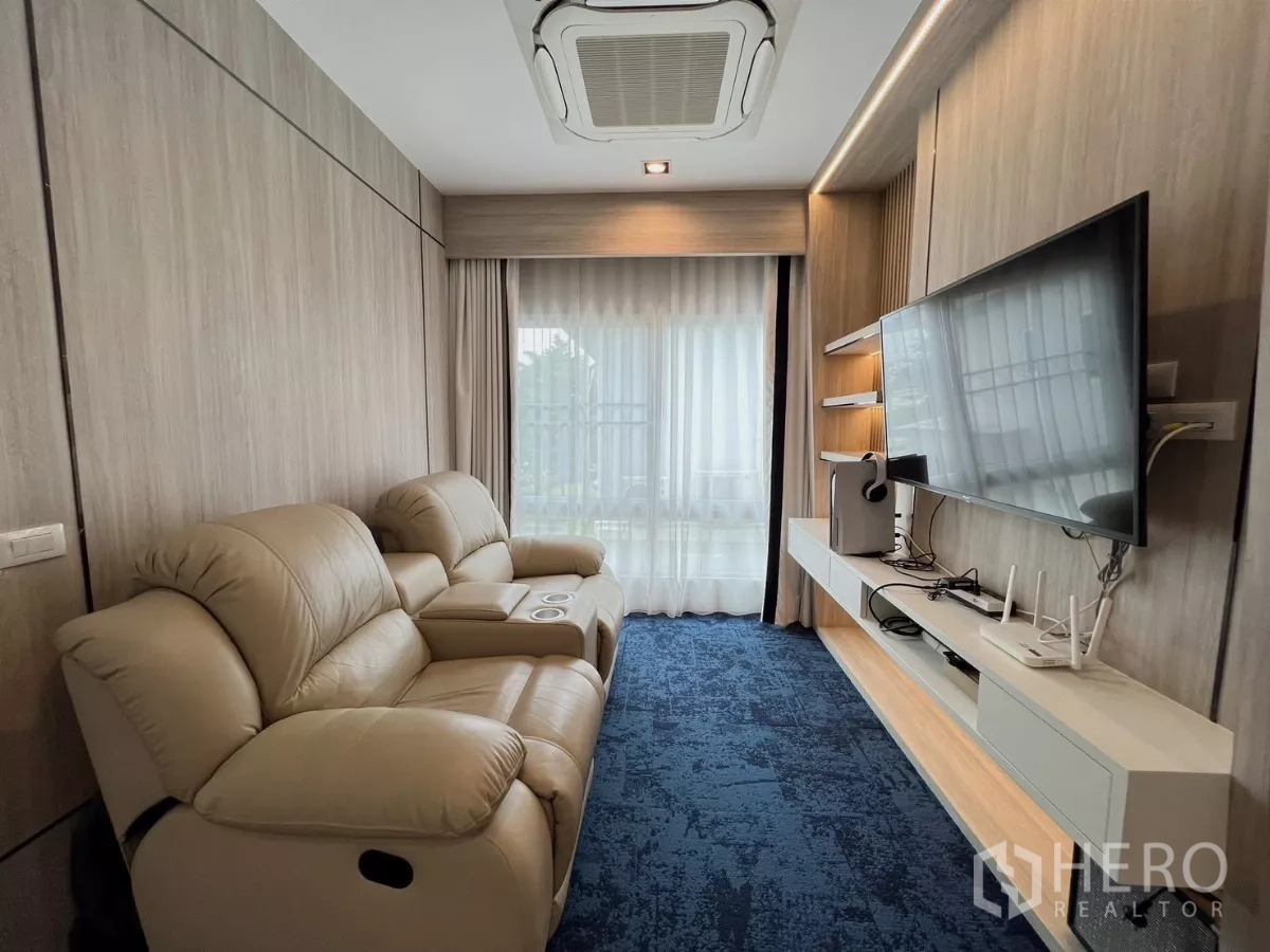 Detached House for rent or sale in Khlong Luang, Pathum Thani - Cozy media room with reclining sofas, wall-mounted TV and blue carpet.