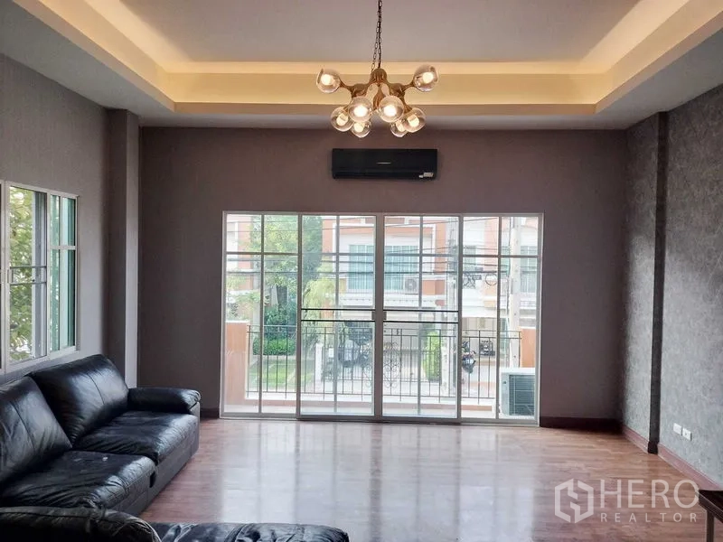 Townhouse for rent in Bueng Kum, Bangkok - Spacious living room with sliding doors to a balcony, chandelier and leather sofa.