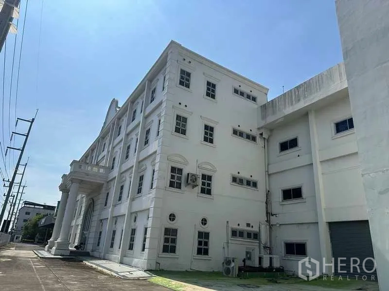 Factory for rent or sale in Thanyaburi, Pathum Thani - Four-storey white factory office facade with classical columns and a side loading bay under a clear sky.