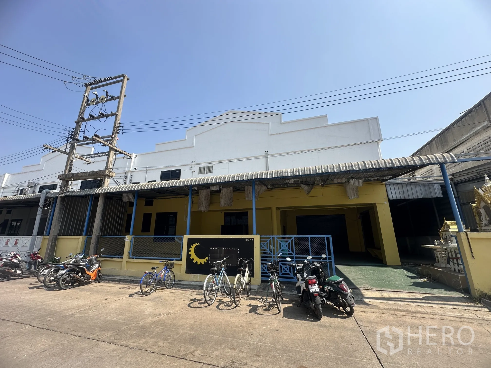工厂 for rent in Lat Lum Kaeo, Pathum Thani - 黄色工厂外立面，带大门与遮雨棚，前方停放自行车与摩托车。