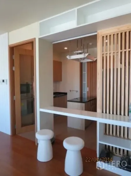 Condominium for rent in Bang Rak, Bangkok - Breakfast bar with two stools separating the kitchen and living area in light wood finishes.