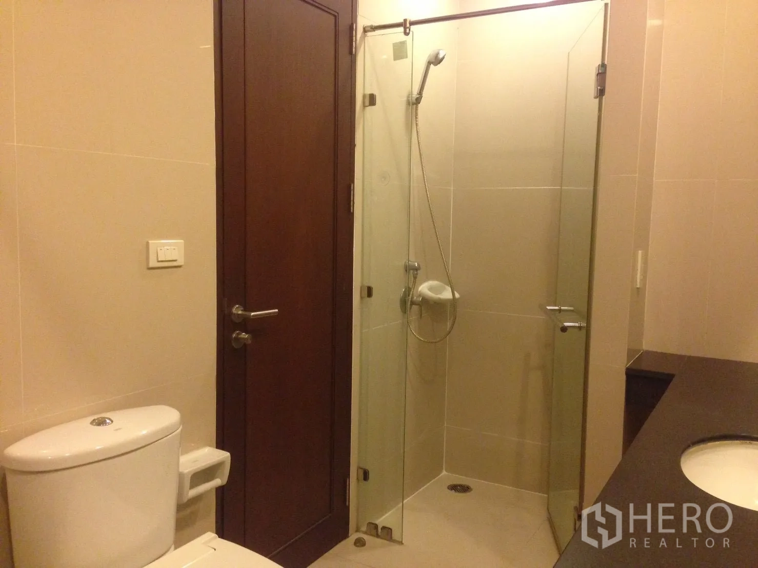 公寓 出租在Watthana, Bangkok - 卫生间配玻璃淋浴间、台面与马桶，浅色瓷砖。