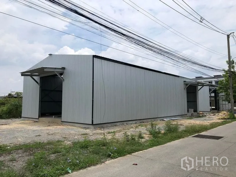 Warehouse for rent in Bang Yai, Nonthaburi - Side view of long metal‑clad warehouse with dual entrances along a local road.