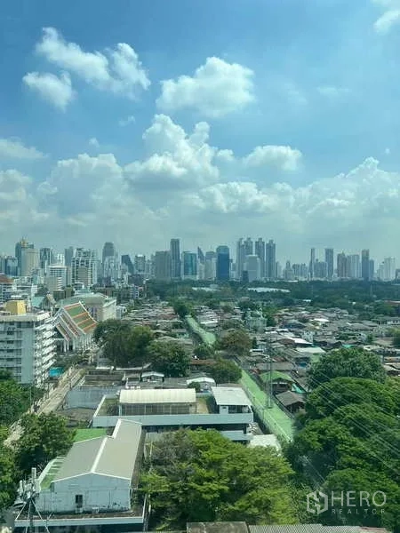 房间 出租在Pathum Wan, Bangkok - 高楼层视野，可见曼谷天际线与绿地，蓝天白云。