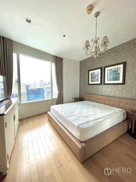 Condominium for rent in Watthana, Bangkok - Sunlit bedroom with upholstered bed, chandelier and wide city-view window.