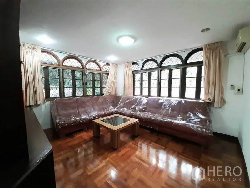 Detached House for rent in Watthana, Bangkok - Bright lounge with wraparound arched windows and a large sectional sofa.