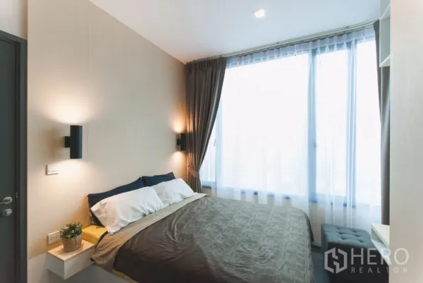 Condominium for rent in Watthana, Bangkok - Bright bedroom with queen bed, wall sconces and large window with sheer curtains.