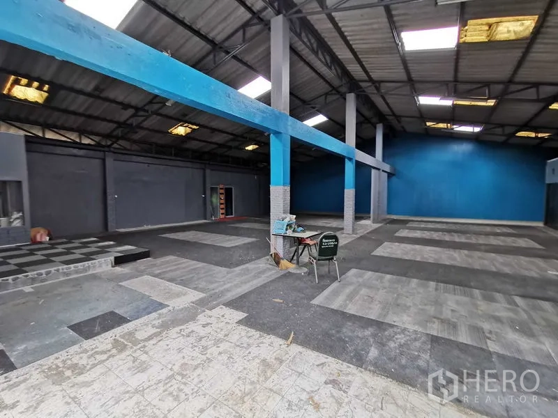 Warehouse for rent in Nonthaburi - Large warehouse floor with blue beams, a small raised platform and concrete flooring.