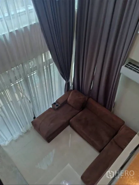 Detached House for rent in Thanyaburi, Pathum Thani - Double-height living room view showing a brown sectional sofa and tall drapes.
