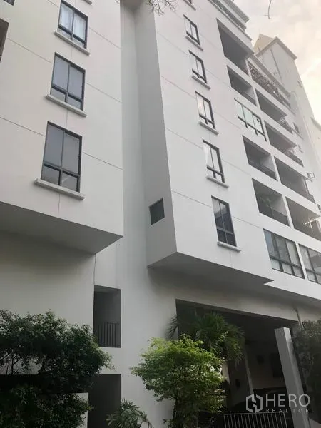 Condominium for sale - Exterior view of a mid-rise white condominium with balconies and greenery.