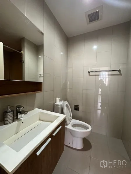 Condominium for rent in Watthana, Bangkok - Modern tiled bathroom with wide vanity, mirror cabinet, and toilet.