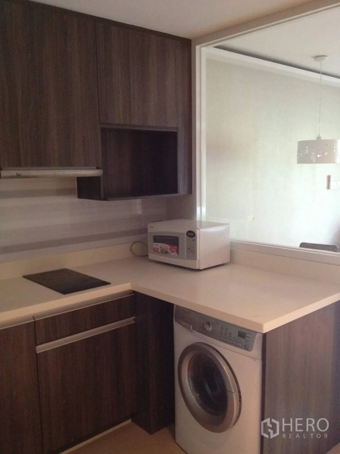 Condominium for rent in Khlong Toei, Bangkok - Compact L-shaped kitchen with washing machine, microwave and dark wood cabinets.