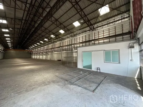 Warehouse for rent in Lam Luk Ka, Pathum Thani - Spacious warehouse interior with high steel truss roof, skylights, concrete floor, and a glass-front office room.