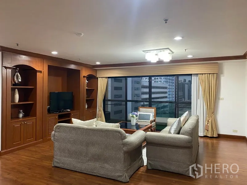 Condominium for rent in Watthana, Bangkok - Living area with built-in wood TV cabinetry, sofa set and large windows overlooking the city skyline.