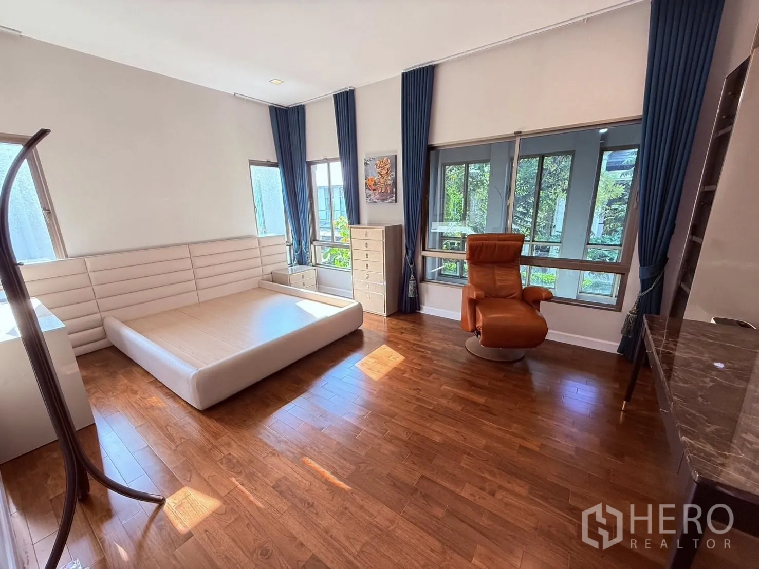 Detached House for rent or sale in Prawet, Bangkok - Large bedroom with platform bed frame, recliner chair, multiple windows, and wood flooring.
