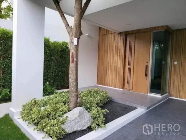 独立式住宅 出租在Saphan Sung, Bangkok - 有顶入户门廊，竖向木饰面与玻璃入户门，配景观树与石景花坛。