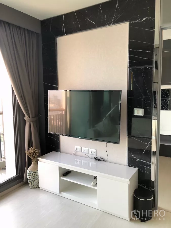 Condominium for rent in Khlong Toei, Bangkok - TV console beneath large screen beside a floor-to-ceiling window.