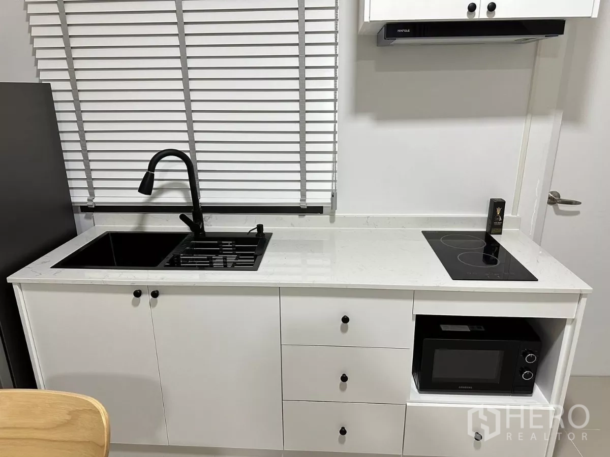 Townhouse for rent in Bang Phli, Samut Prakan - Modern white kitchen featuring a black sink, gas hob, electric cooktop and built‑in microwave.