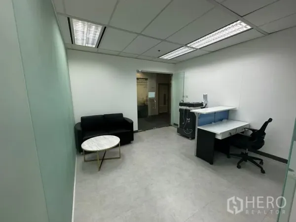 Office Space for rent - Reception and workstation area with black sofa, round marble coffee table and glass partition walls.