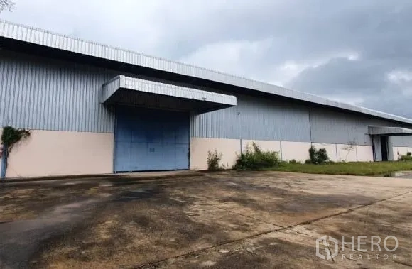 货栈 出租在Chaloem Phra Kiat, Nakhon Ratchasima - 带大号蓝色卷帘门的装卸口，金属波纹墙体。