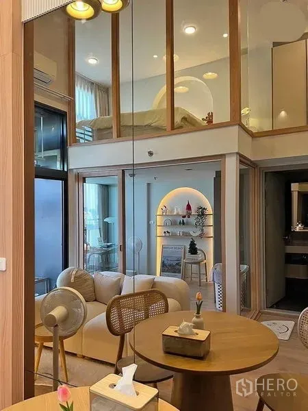 Condominium for rent in Huai Khwang, Bangkok - Loft-style condo interior with a glass-partition mezzanine bedroom above a cozy living and dining area.