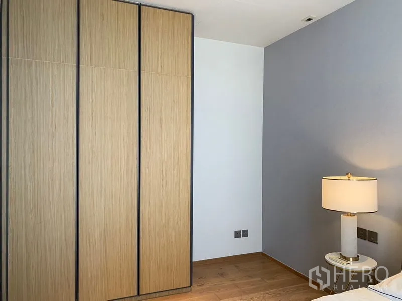 Condominium for rent in Khlong Toei, Bangkok - Corner of room with built-in wooden wardrobes and table lamp against an accent wall.