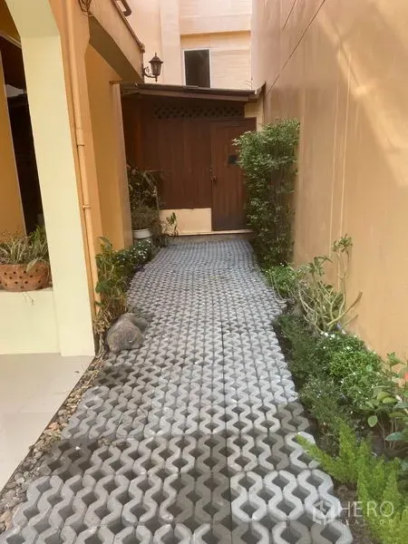 Detached House for rent in Watthana, Bangkok - Paved side walkway with greenery leading to a wooden door.