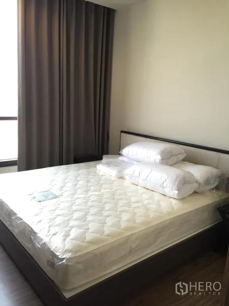 Condominium for rent in Watthana, Bangkok - Bright bedroom with double bed, pillows, bedside table and thick grey curtains.