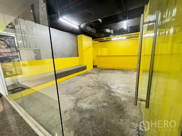 Retail Space for rent - Entrance view through clear glass doors into concrete-floored shop with yellow feature walls.