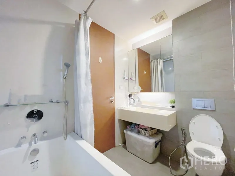 Condominium for sale in Khlong Toei, Bangkok - Bathroom featuring a bathtub with shower, wide vanity and toilet in soft grey tones.