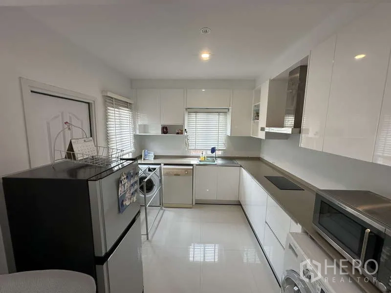 Detached House for sale in Sai Mai, Bangkok - Modern white L-shaped kitchen with built-in cupboards and appliances.