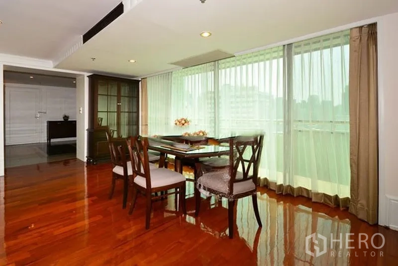 Apartment for rent in Khlong Toei, Bangkok - Dining corner by floor-to-ceiling windows with city view and a glass cabinet on hardwood flooring.
