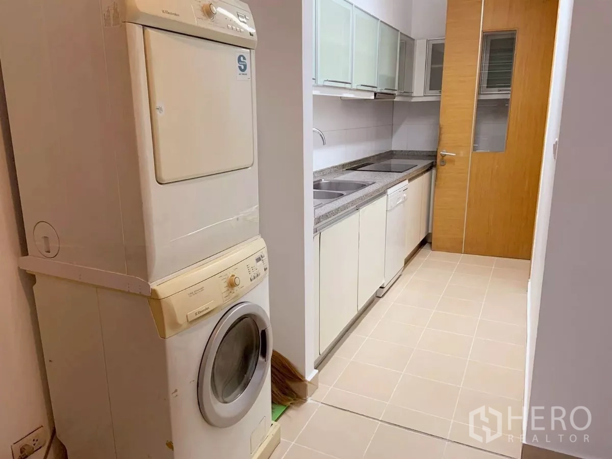 Condominium for rent in Khlong Toei, Bangkok - Utility area with stacked washer and dryer next to a closed kitchen.
